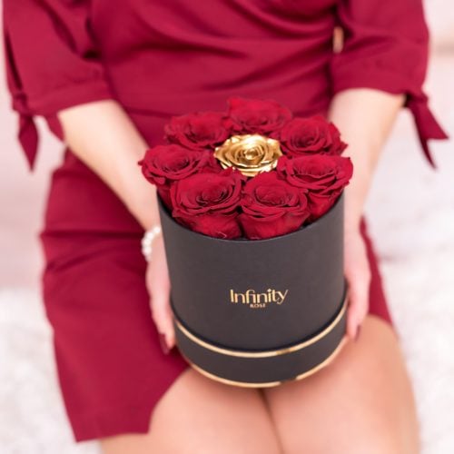 Kobieta w czerwonj sukience trzymająca w dłoniach czarny flower box Infinity Rose z wiecznymi różami w kolorze czerwonym i złotym